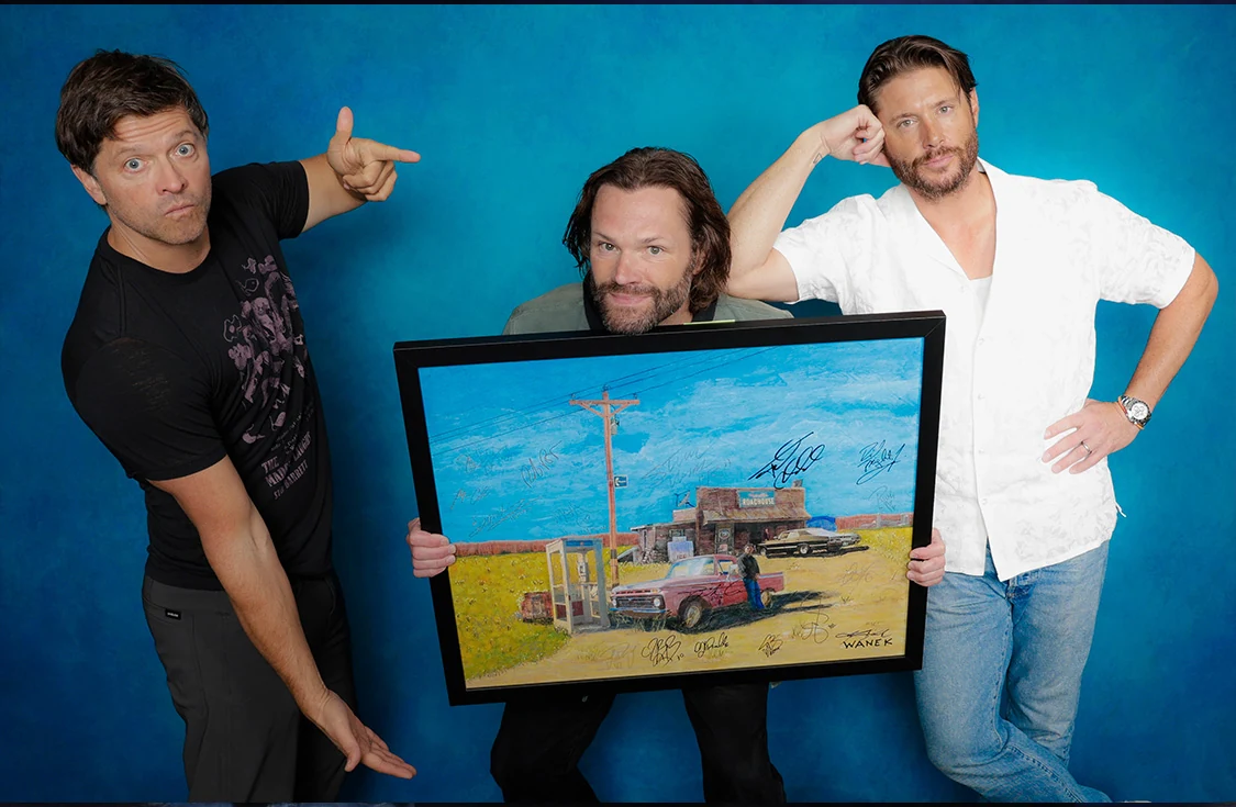 Misha Collins, Jared Padalecki, and Jensen Ackles holding a signed Jerry Wanek Roadhouse painting