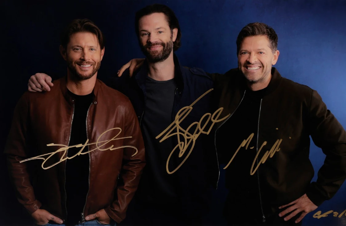 Jensen Ackles, Jared Padalecki, and Misha Collins smiling together, autographed in gold ink