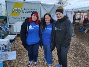 3 women stand next to each other in front of a white transporter. All wear Random Acts clothing and warm coats.