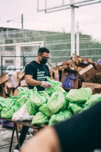 volunteer sorting donations with empty boxes in a pile behind him and a pile of green plastic bags on a table in front of him