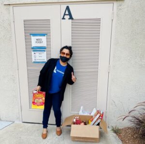 a person wearing a blue shirt, black pants, and a black mask next to a box filled with food donations